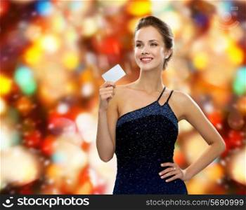 shopping, wealth, holidays and people concept - smiling woman in evening dress holding credit card over red lights background