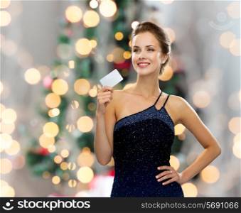 shopping, wealth, holidays and people concept - smiling woman in evening dress holding credit card over christmas tree lights background