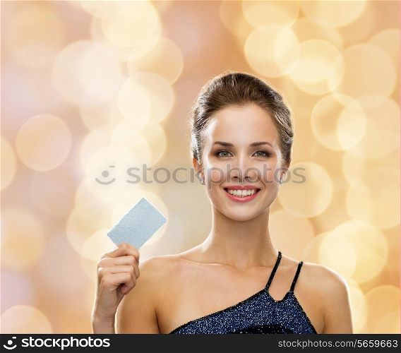 shopping, wealth, luxury, holidays and people concept - smiling woman in evening dress holding credit card over beige lights background