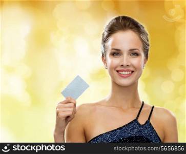 shopping, wealth, money, holidays and people concept - smiling woman in evening dress holding credit card over yellow lights background