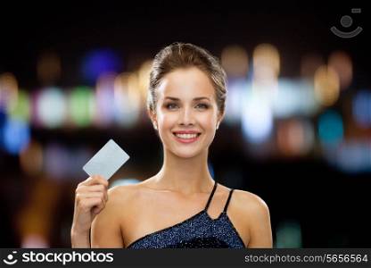 shopping, wealth, money, luxury and people concept - smiling woman in evening dress holding credit card over night lights background