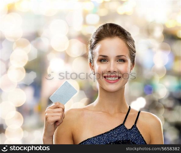 shopping, wealth, money, luxury and people concept - smiling woman in evening dress holding credit card over holidays lights background