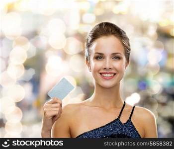 shopping, wealth, money, luxury and people concept - smiling woman in evening dress holding credit card over holidays lights background