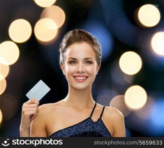 shopping, wealth, money, luxury and people concept - smiling woman in evening dress holding credit card over night lights background