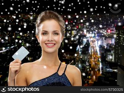 shopping, wealth, money, luxury and people concept - smiling woman in evening dress holding credit card over snowy night city background