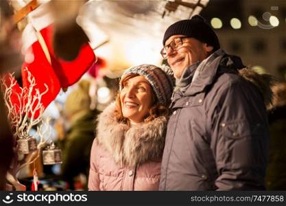shopping, winter holidays and people concept - happy senior couple at christmas market souvenir shop on town hall square in tallinn, estonia. senior couple at christmas market souvenir shop