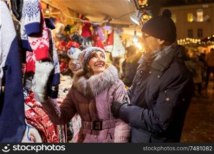 shopping, winter holidays and people concept - happy senior couple at christmas market clothing shop on town hall square in tallinn, estonia. senior couple at christmas market clothing shop