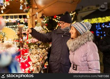 shopping, winter holidays and people concept - happy senior couple at christmas market souvenir shop stall on town hall square in tallinn, estonia. happy senior couple hugging at christmas market