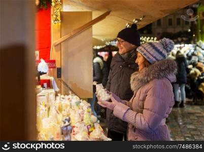 shopping, winter holidays and people concept - happy senior couple at christmas market souvenir shop window on town hall square in tallinn, estonia. happy senior couple hugging at christmas market