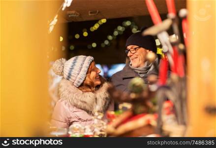 shopping, winter holidays and people concept - happy senior couple at christmas market souvenir shop on town hall square in tallinn, estonia. senior couple at christmas market souvenir shop