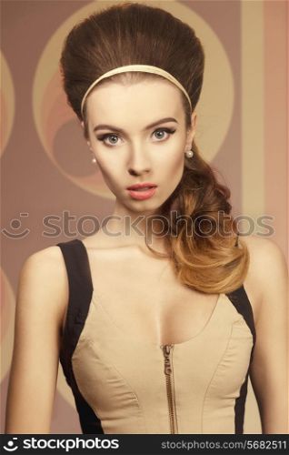 Short portrait of beautiful girl in fitted cream and black dress is standing in front of camera. She has got big blue eyes, brown big hairstyle and she is wearing hairband and pearls on her ears. She has got red lips and highlighted eyes.