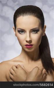 Short portrait of beautiful, young girl on grey background. She has long, straight, brown hair clipped in ponytail, purple lips and hypnotizing eyes.