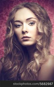 Short portrait of blonde beautiful young girl with long curly hair on pink backgroung is looking in camera