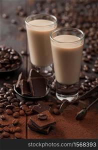 Shot glasses of Irish cream baileys liqueur with coffee beans and powder with dark chocolate on dark wood background. Macro