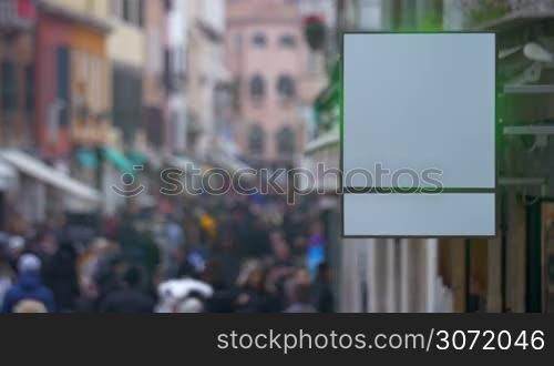Shot of a blank shop signboard with city street crowded with people on the background.