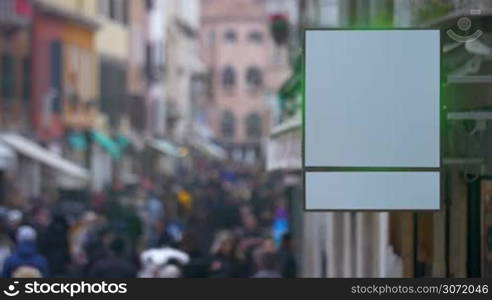 Shot of a blank shop signboard with city street crowded with people on the background.