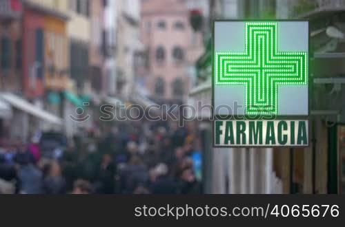 Shot of a lightbox of a drugstore in Italy. City street crowded with people is on the background.