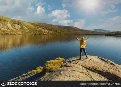 Shot of a woman hiking near a beautiful lake with arms raised