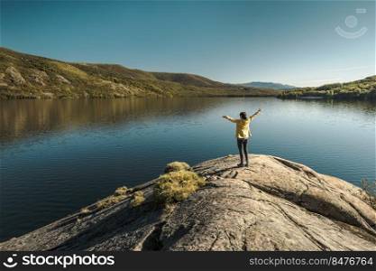 Shot of a woman hiking near a beautiful lake with arsm raised