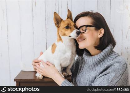 Shot of attractive young woman embraces her favourite dog, touches with nose, expresses great love to pet. Loyal dog has good relationships with host. Friendship, relations, animals and people