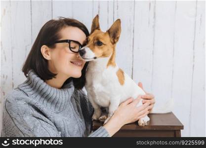 Shot of attractive young woman embraces her favourite dog, touches with nose, expresses great love to pet. Loyal dog has good relationships with host. Friendship, relations, animals and people