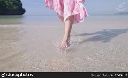 Shot of Female legs and feet walking on white sand beach on sunny day. Slim pretty girl kick and play with sea water and waves. summer vacation. Low camera angle, slow motion. Horizon seascape sky