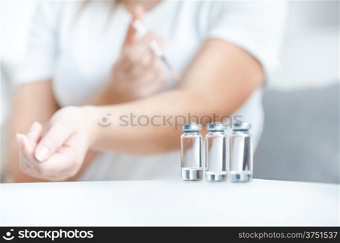Shot of glass bottles with insulin against woman doing prick