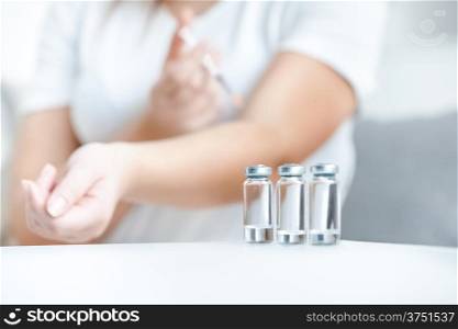 Shot of glass bottles with insulin against woman doing prick