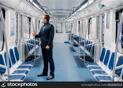 Shot of man who doesnt work at distance during quarantine, wears face mask to avoid coronavirus infection, poses in empty underground carriage with no people. Health awareness for pandemic protection