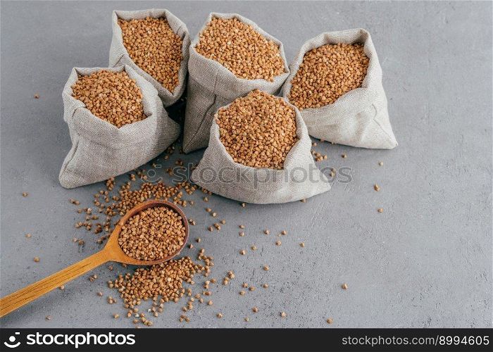 Shot of raw buckwheat groats in sacks and wooden spoon against grey background with copy space for text. Healthy diet. Selective focus