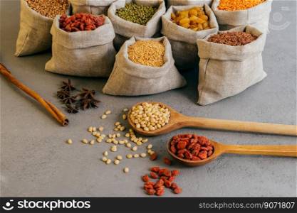 Shot of small bags with colorful cereals, nutritious legumes, star anise near, two wooden spoons with red goji berries. Raw products