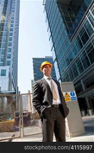Shot showing a man dressed in a suit and hard hat on a costruction site in a modern city environment.