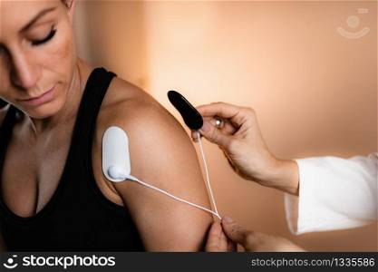 Shoulder Physical Therapy with TENS Electrode Pads, Transcutaneous Electrical Nerve Stimulation. Therapist Positioning Electrodes onto Patient&rsquo;s Shoulder. Shoulder Physical Therapy with TENS Electrode Pads, Transcutaneous Electrical Nerve Stimulation