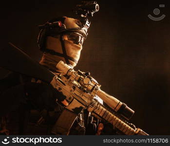 Shoulder portrait of army elite troops sniper, anti-terrorist tactical team marksman wearing helmet with thermal imager, hiding face behind mask, armed rifle with optical scope, studio shoot on black. Army elite troops sniper low key studio portrait