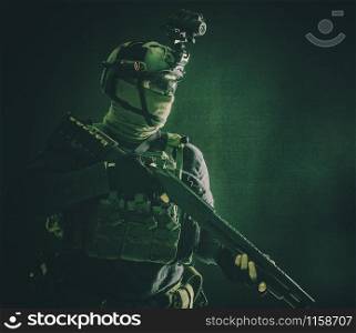 Shoulder portrait of army elite troops soldier, anti-terrorist tactical team wit shotgun, helmet with thermal imager, hiding face behind mask, armed rifle with optical scope, studio shoot on black. Army elite troops soldier low key studio portrait