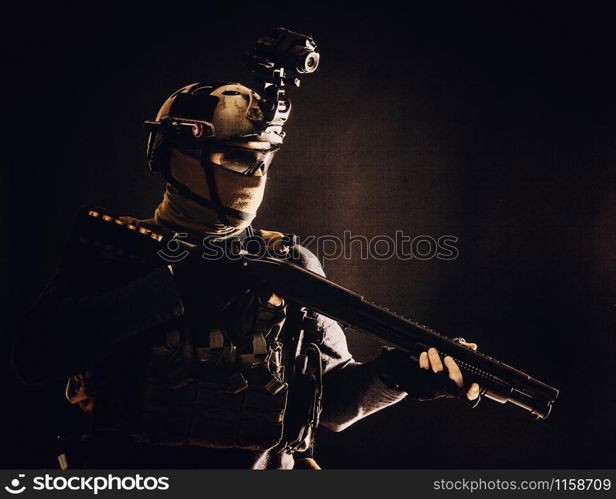 Shoulder portrait of army elite troops soldier, anti-terrorist tactical team wit shotgun, helmet with thermal imager, hiding face behind mask, armed rifle with optical scope, studio shoot on black. Army elite troops soldier low key studio portrait