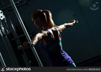 Shoulder workout. Image of fitness girl in gym exercising with dumbbells