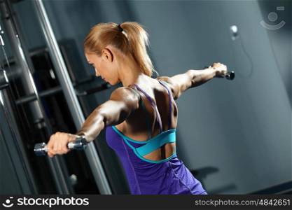 Shoulder workout. Image of fitness girl in gym exercising with dumbbells