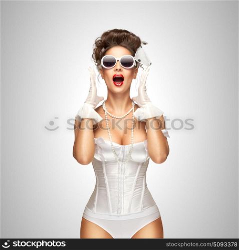 Shouting loudly.. Sexy pinup bride in a vintage wedding corset with sunglasses on grey background.