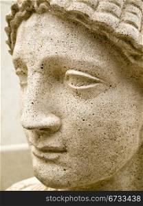 Shown in proflle, the face of a classical nymph or goddess on a concrete statue in an outside park.