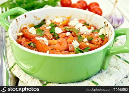 Shrimp and tomatoes baked with feta cheese in a roasting pan on a kitchen towel, parsley and garlic on a wooden boards background