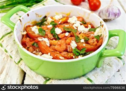 Shrimp and tomatoes baked with feta cheese in a roasting pan on a towel, parsley and garlic on a wooden boards background