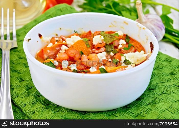 Shrimp and tomatoes baked with feta cheese in a white bowl on a green kitchen towel, parsley and garlic, fork on the background of wooden boards