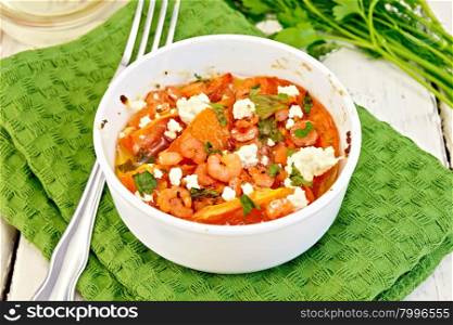 Shrimp and tomatoes baked with feta cheese in a white bowl on a towel, parsley and fork on a wooden boards background