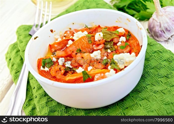 Shrimp and tomatoes baked with feta cheese in a white bowl on a green towel, parsley and garlic, fork on the background of wooden boards