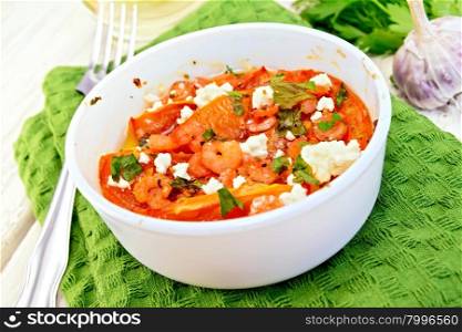 Shrimp and tomatoes baked with feta cheese in a white bowl on a green towel, parsley and garlic, fork on the background of wooden boards