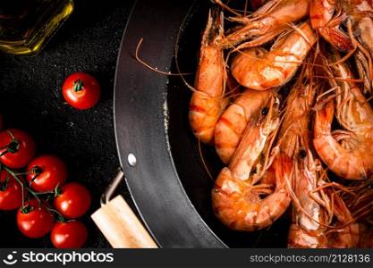 Shrimp boiled in a saucepan with a sprig of tomatoes. On a black background. High quality photo. Shrimp boiled in a saucepan with a sprig of tomatoes.