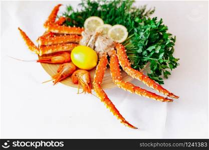 Shrimp, crab, lemon and greens on a plate on a white background.