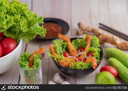 Shrimp deep fried batter placed on salad and tomatoes in a wooden bowl.