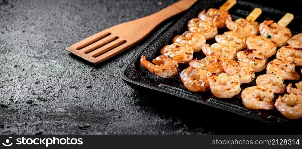 Shrimp on skewers are grilled in a grill pan. On a black background. High quality photo. Shrimp on skewers are grilled in a grill pan.